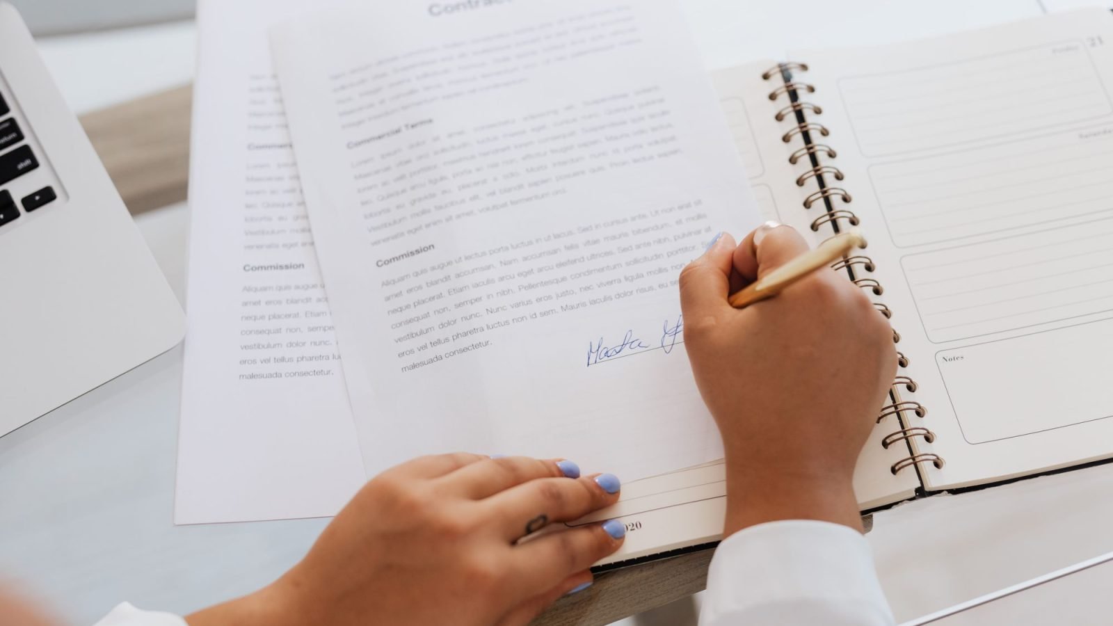 Hands signing a contract on a desk with office supplies